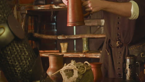 attendant pours drink to knight mug in tavern closeup. careful innkeeper gives jug of wine to warrior in armour at medieval inn. adventurer visits pub