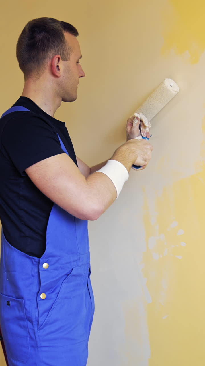 Young worker painting wall in room. Offering professional painting services. Vertical video