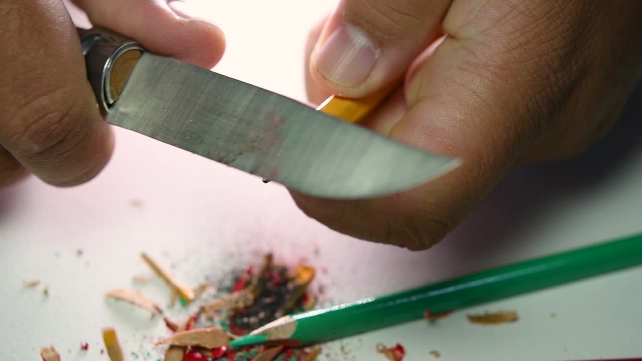 Opptak av hender som sakte spisser en blyant og noen fargeblyanter med en skarp kniv