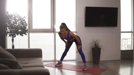 Slender-caucasian-lady-is-doing-sports-at-home-stretching-body,-arms-and-legs-leaning-to-the-floor-enjoying-activity-and-healthy-lifestyle.-Sport-and-millennials-concept