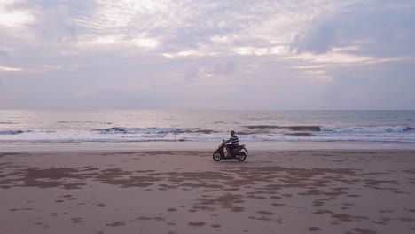 Vista-De-Drones-De-Una-Motocicleta-Yendo-Rápido-En-La-Playa-Al-Atardecer