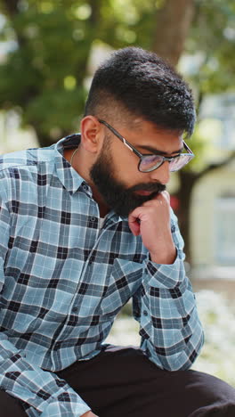 Sad-unhappy-frustrated-Indian-man-sitting-alone-in-city-street,-feeling-bad,-annoyed,-grief,-problem