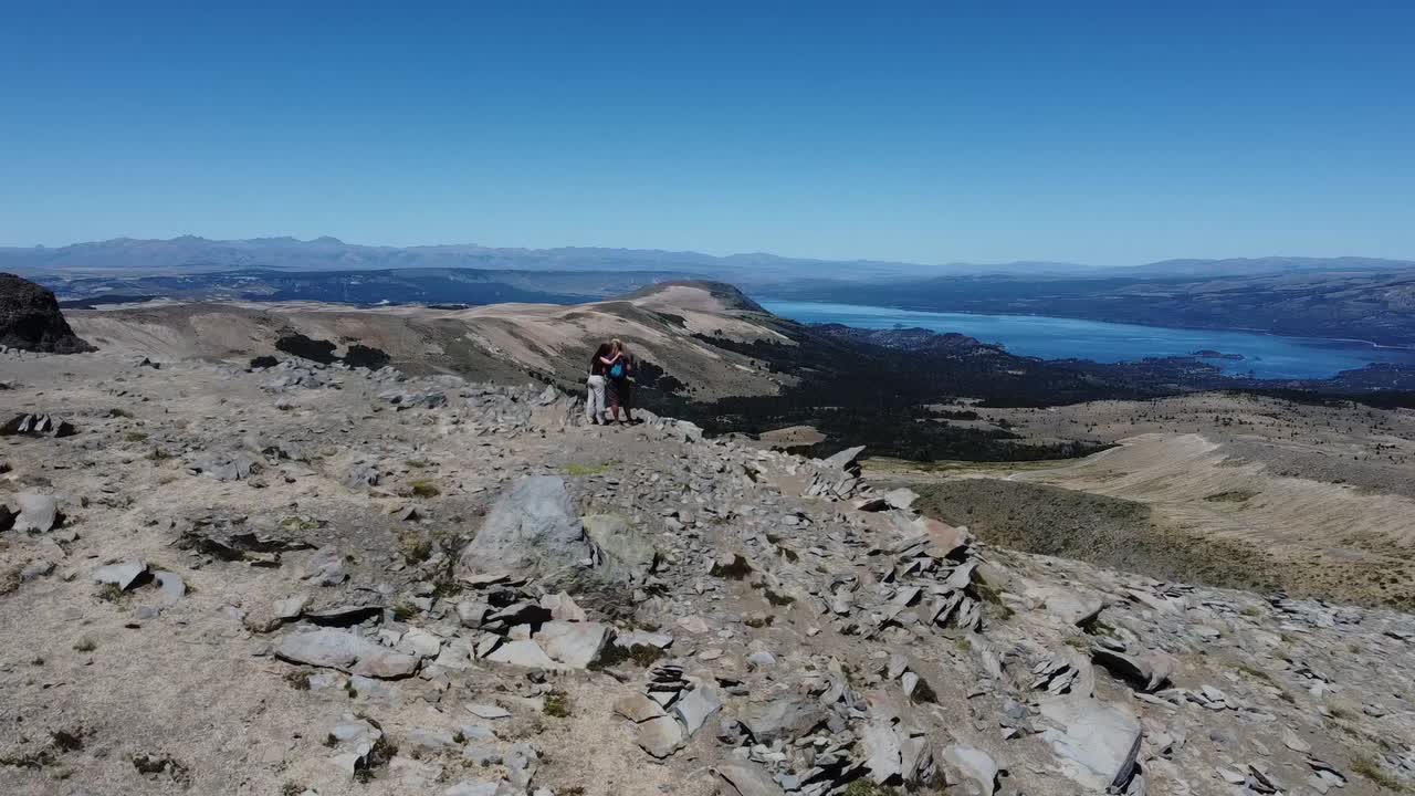 aereal camera passing over a couple standing in the edge of an old volcano looking at the world itself. captured in Volcan Vatea Mahuida in the border between Argentina and Chile