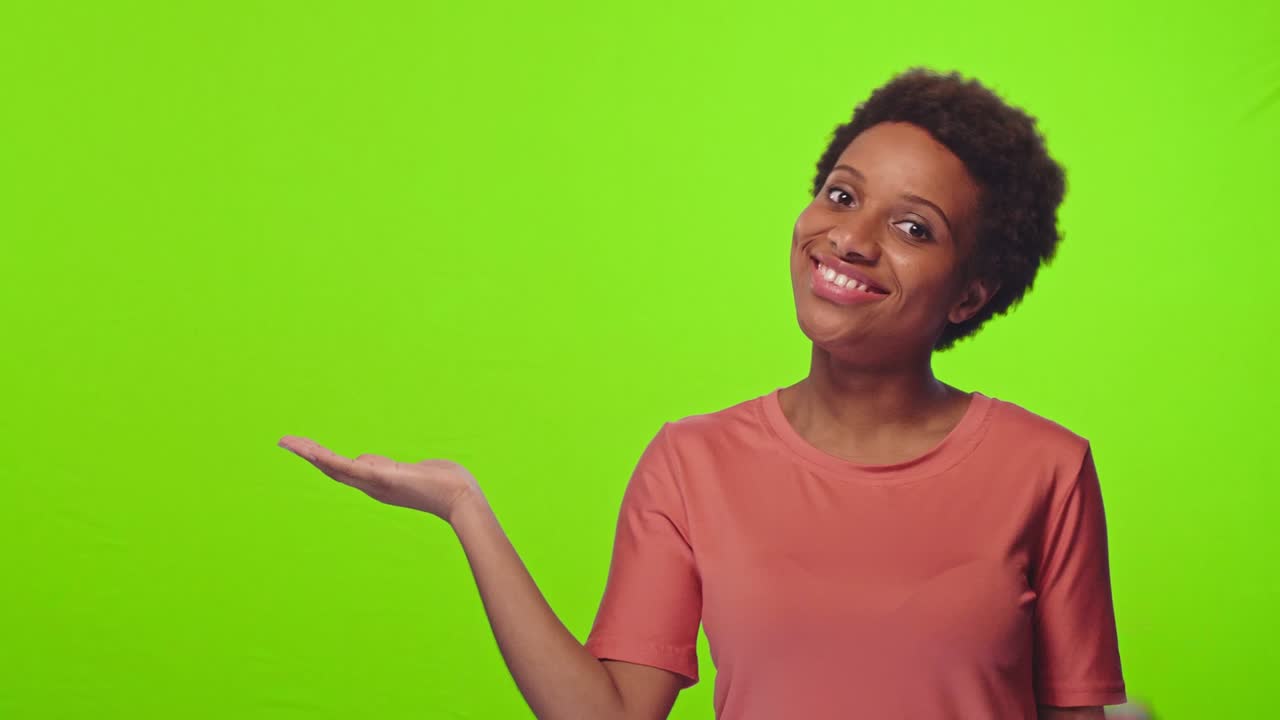 African woman raises palm near shoulder, holds copy space, smiles, chroma key
