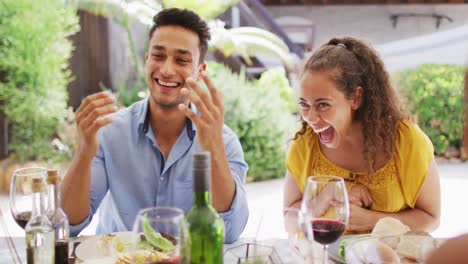 Diverse-couple-laughing-with-friends-at-dinner-party-on-patio