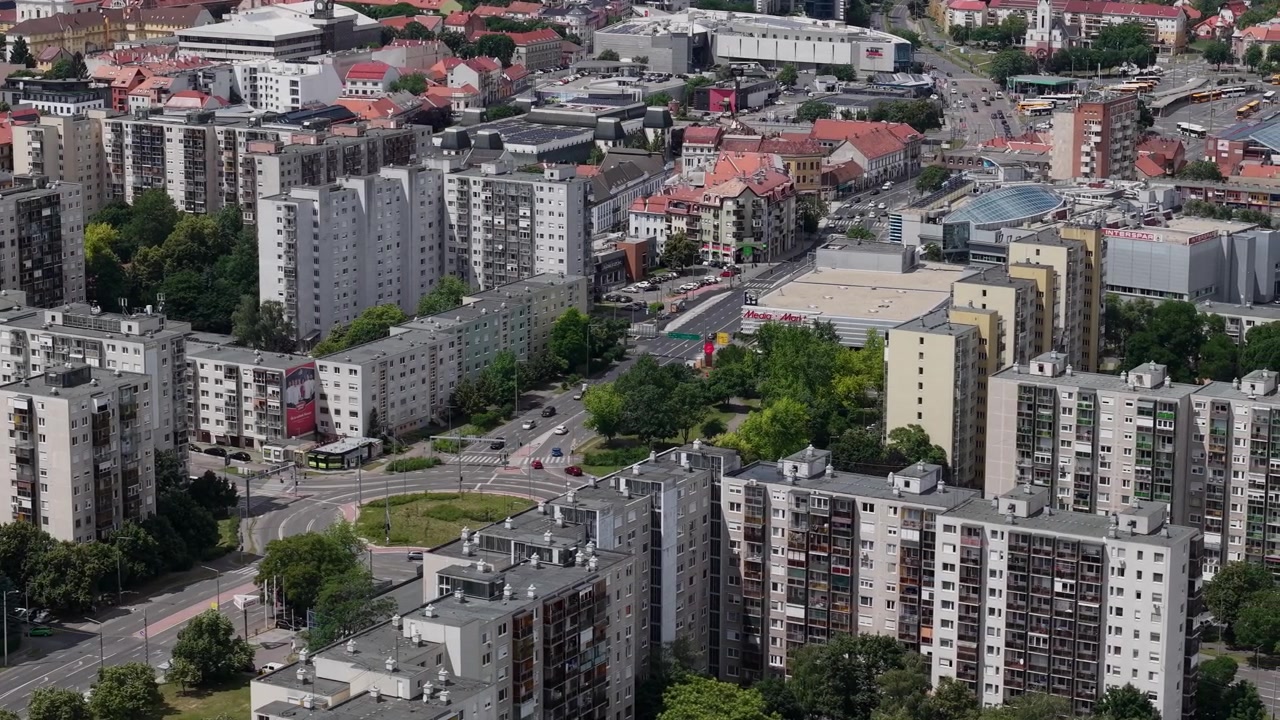 Widok z lotu ptaka przedstawia wieżowce z wielkiej płyty i ruchliwe rondo w gęsto zaludnionej węgierskiej dzielnicy mieszkaniowej.