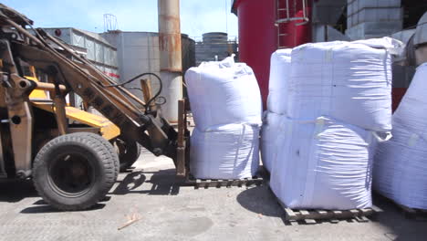 side shot of a tractor backhoe forklift handled by a worker move in and carry up a heavy bale of mass inside the factory area