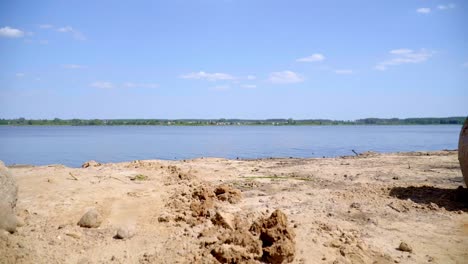 Sand-and-huge-stones-on-shore-of-lake-near-village.-Butterflies-fly-near-lake