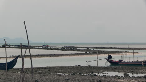 small thai tourist boat enters a small rocky fairway at low tide, on a cloudy day