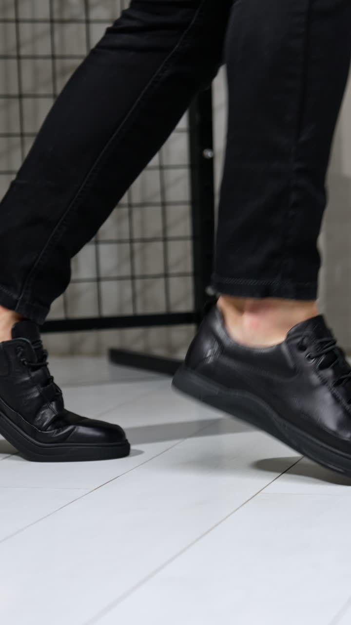 Unrecognized man in black jeans and leather sneakers showing moonwalk. Stylish male footwear demonstration in studio. Vertical video
