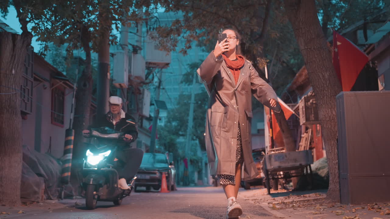 Passeggiata serale in un vicolo, un anziano asiatico cammina attraverso uno stretto hutong, cappotto e sciarpa, debole bagliore di una lampada, bandiere e scooter, foglie cadute sul selciato, illuminazione cinematografica suggestiva, solitudine e quieta riflessione.