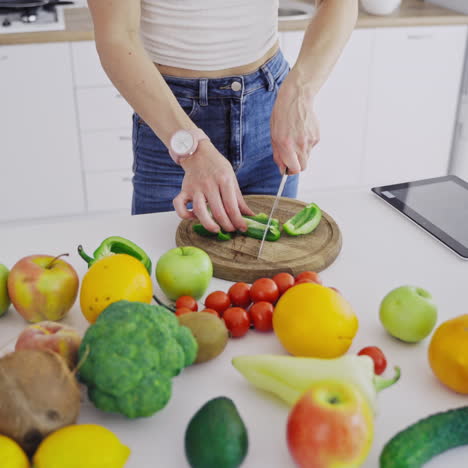 organic vegetables and fruit on the table. woman is cutting green pepper on a wooden board to prepare healthy food. dieting concept.