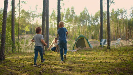 two boys collect sticks in the woods for a large family campfire against the backdrop of a tent and a lake. family is going to light a fire for camping and frying marshmallows