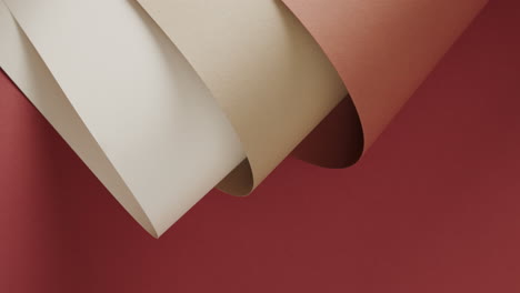 Close-up-of-three-shades-of-brown-rolled-papers-on-red-background-with-copy-space-in-slow-motion