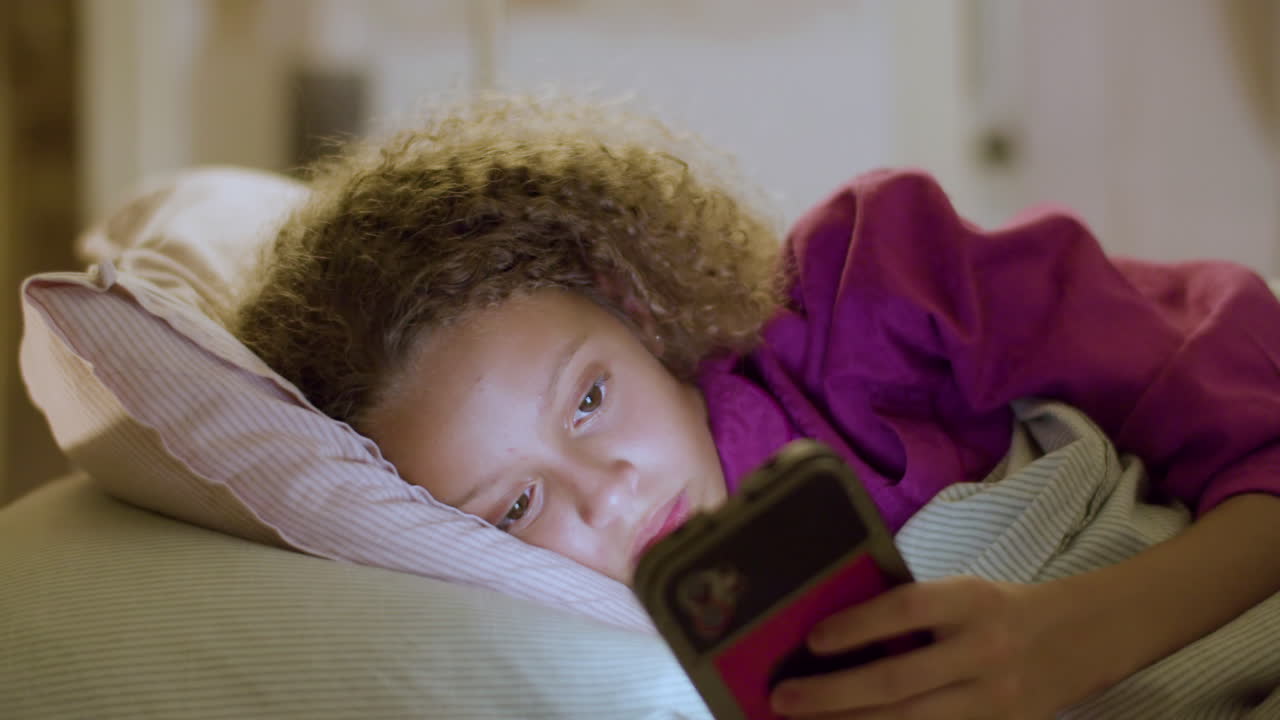 Girl lying in bed, typing on smartphone before falling asleep