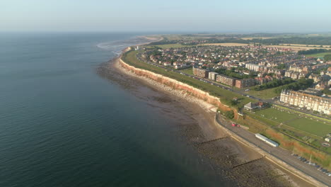 toma aérea de alto establecimiento de los antiguos acantilados anaranjados y blancos de hunstanton con casas y faro en la distancia al atardecer en el norte de norfolk, reino unido