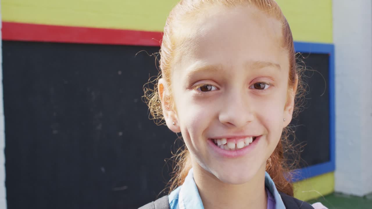 Portrait of happy caucasian schoolgirl looking at camera on playground