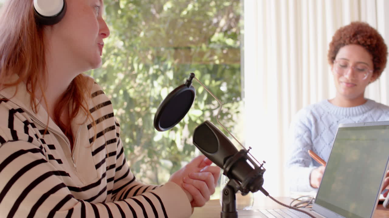 Recording podcast, woman wearing headphones speaking into microphone with friend
