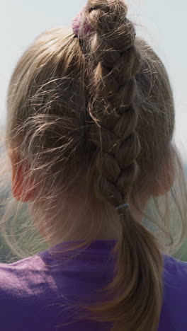 little child with blonde plait looks at distant mountain peak riding cabin of cable way at highland close backside view slow motion