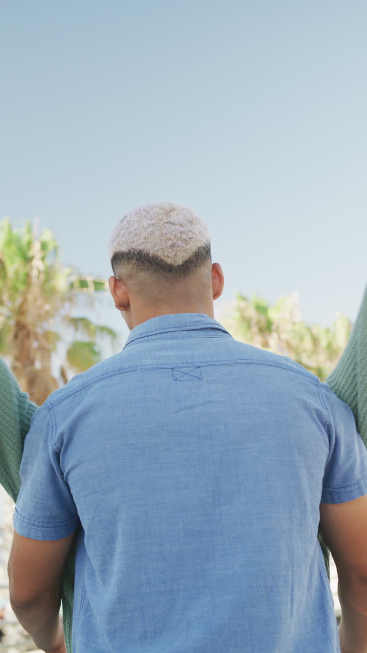Vertical video of happy biracial couple embracing on promenade, in slow motion