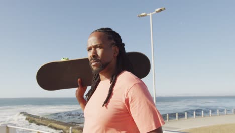 video of african american man holding skateboard by sea