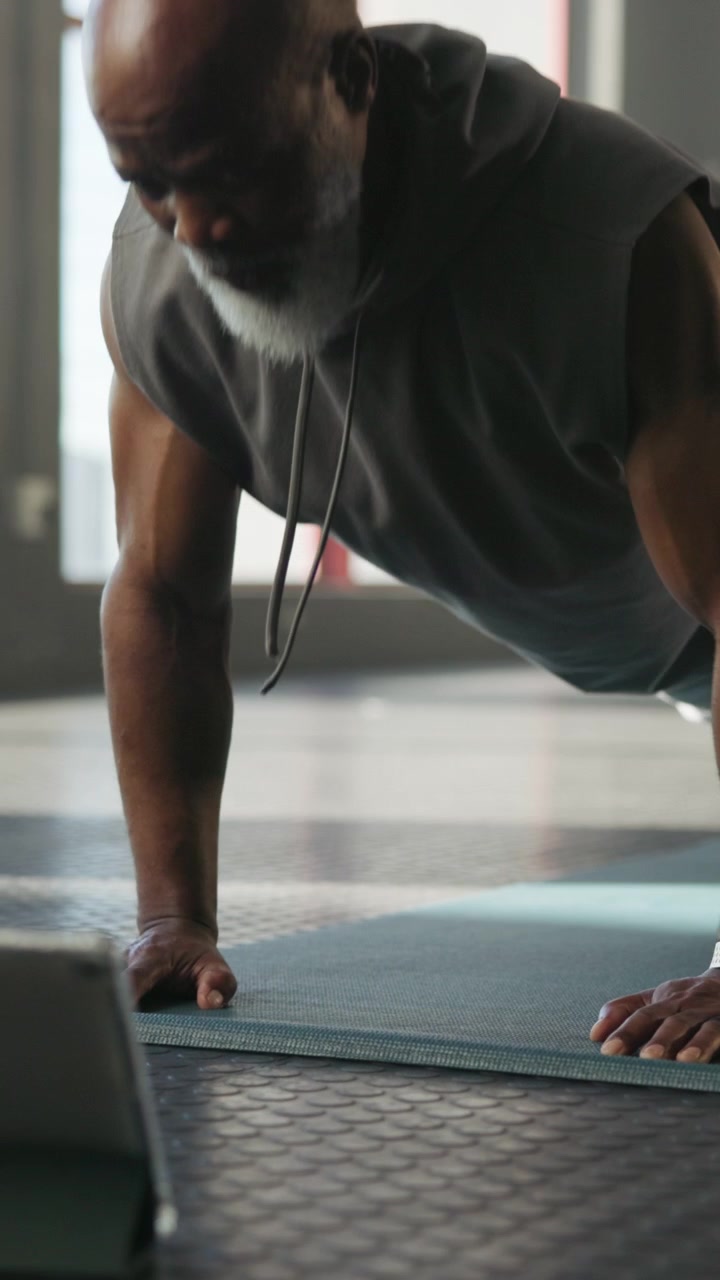 Senior Man Doing Pushups While Watching Online Workout on Tablet