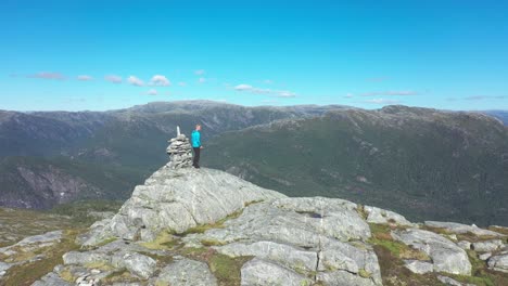 man standing on top of mountain and enjoying beautiful norwegian mountain scenery - forward moving aerial passing close to man and continuing forward into vast landscape - stamneshella bolstadfjord