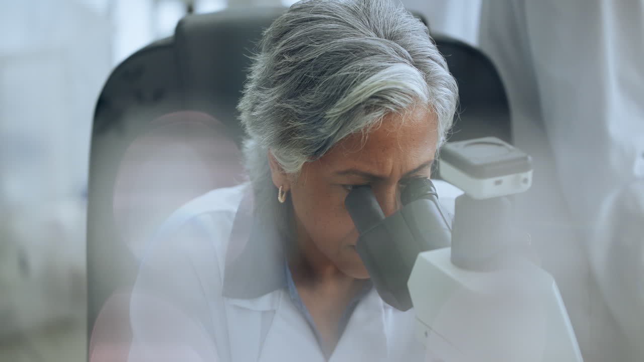 Senior Woman Scientist Looking Through Microscope in Laboratory