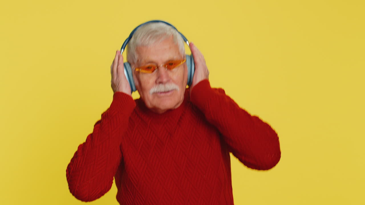 Vecchio anziano elegante che ascolta musica con le cuffie e balla nonno felice pensionato