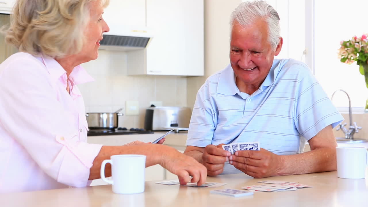 Casal idoso sentado no balcão jogando cartas.