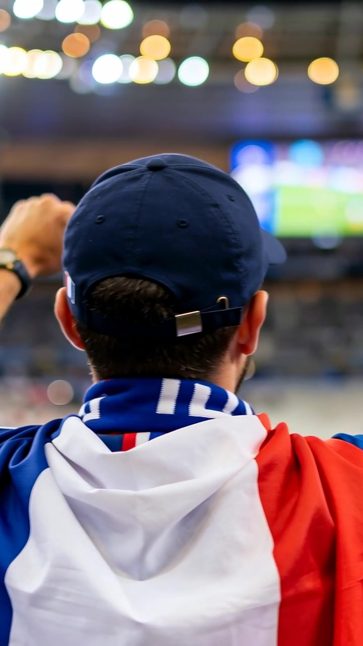 Video verticale: Reagendo a un aggiornamento dello schermo, un tifoso che alza il pugno e si gira nello stadio, con sciarpa con bandiera e cappellino