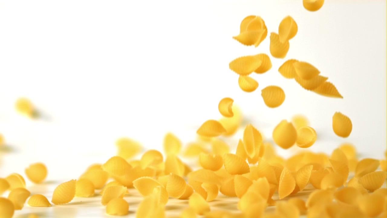 Pasta conchiglie cruda che cade al rallentatore su sfondo bianco.