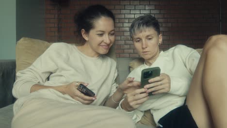 two women sharing a smartphone on a couch