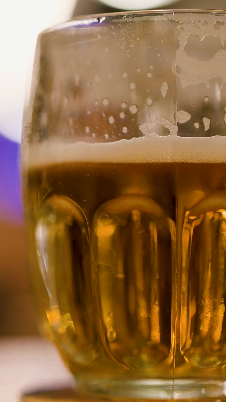 Cerveza lager dorada en vaso texturizado girando sobre una mesa, con iluminación ambiental cálida y poca profundidad de campo.