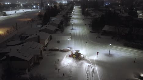 aerial: snow plow clearing snow at night in st-constant, quebec, canada, crane down drone shot