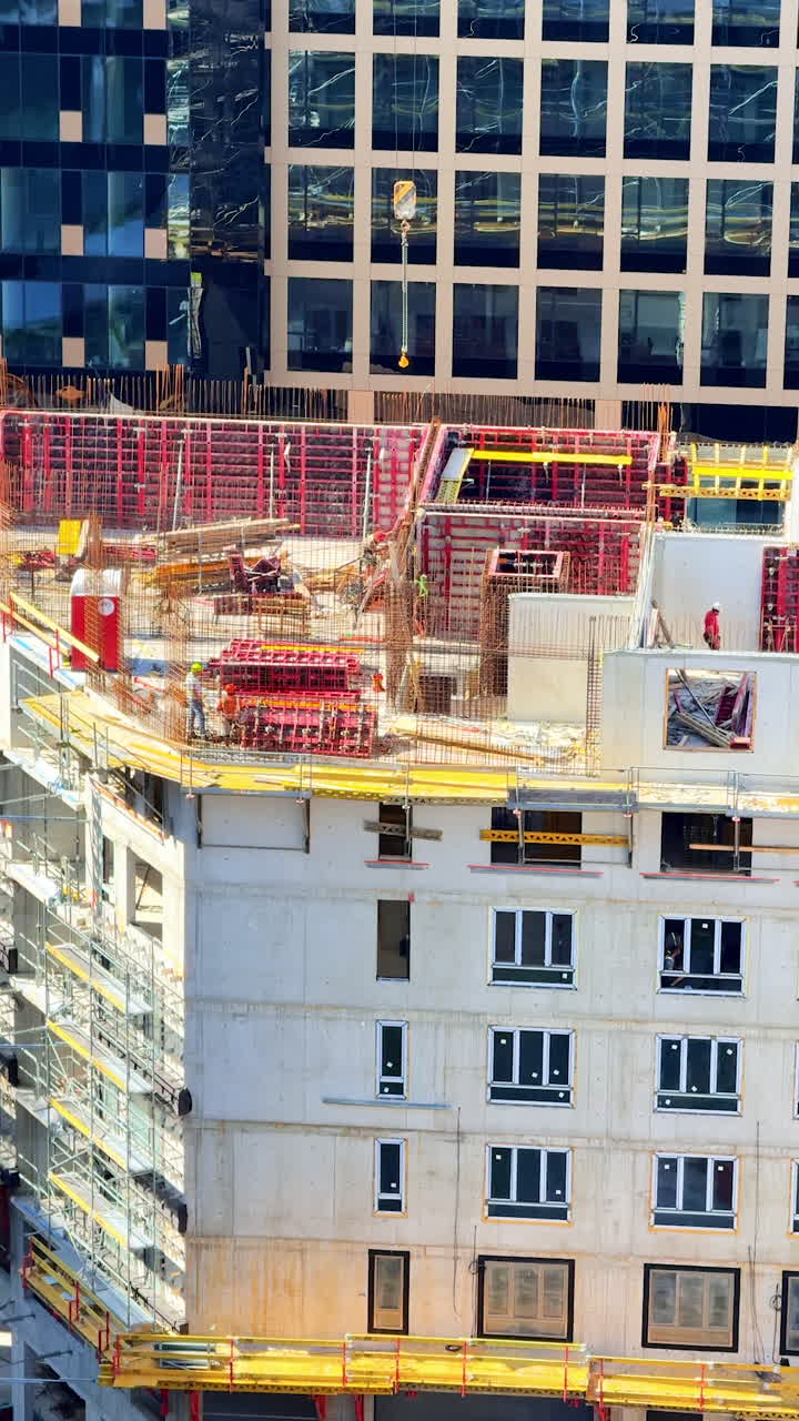 Urban midday construction site. Workers are constructing a high-rise building surrounded by scaffolding and cranes in a bustling urban environment