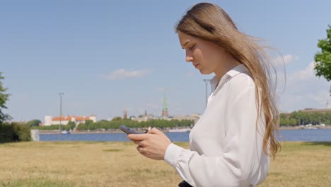 woman in classy clothes typing message on phone, cityscape in background