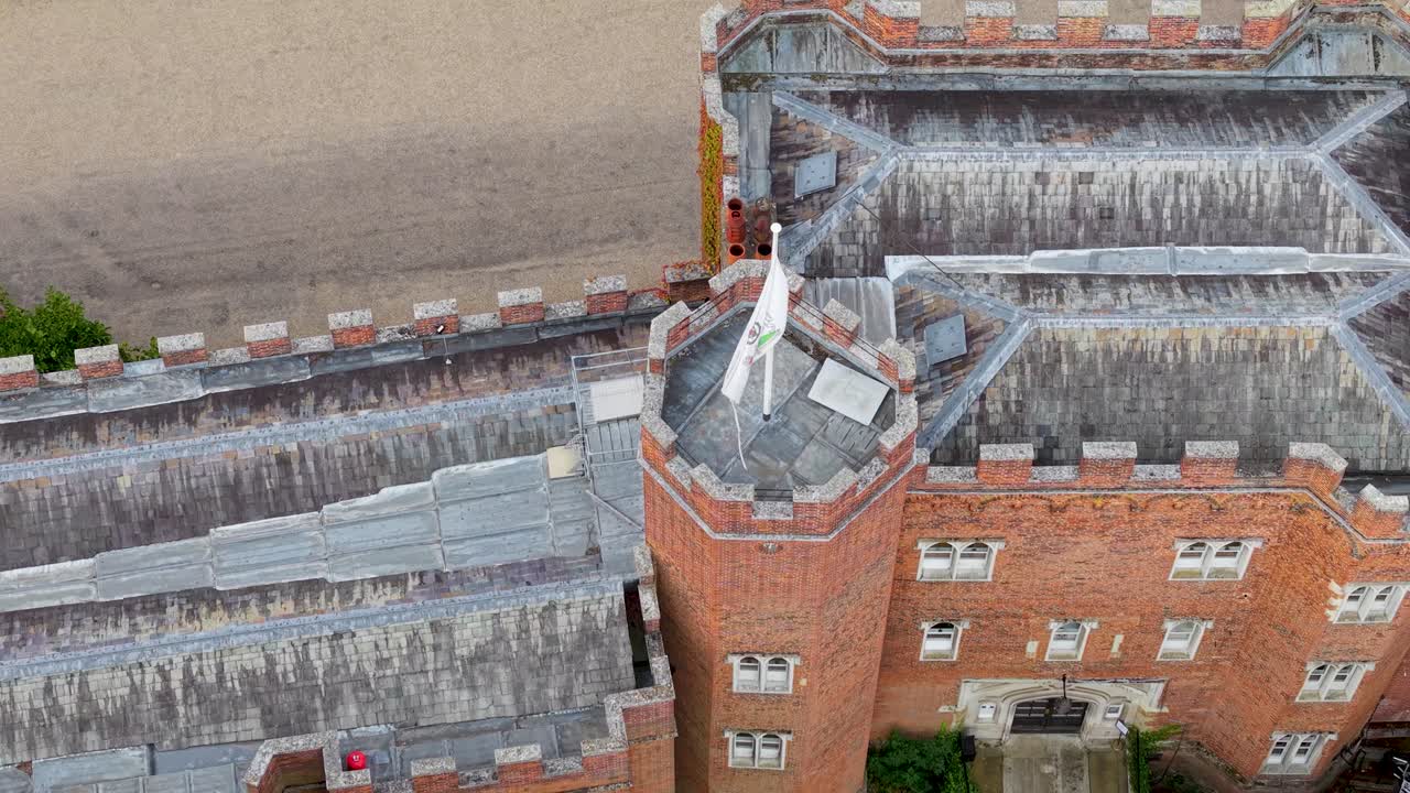 Drone hovers top-down over Hertford Castle, Hertford, showing the flag atop, then pulls back with gimbal tilt to reveal the castle’s front facade and surrounding grounds
