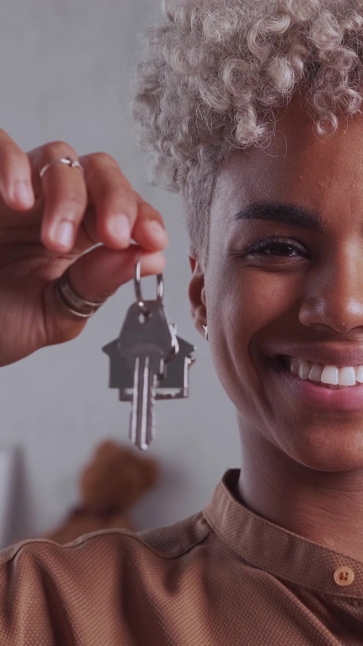 Felice proprietario di casa afroamericano che sorride e mostra una chiave con un portachiavi a forma di casa