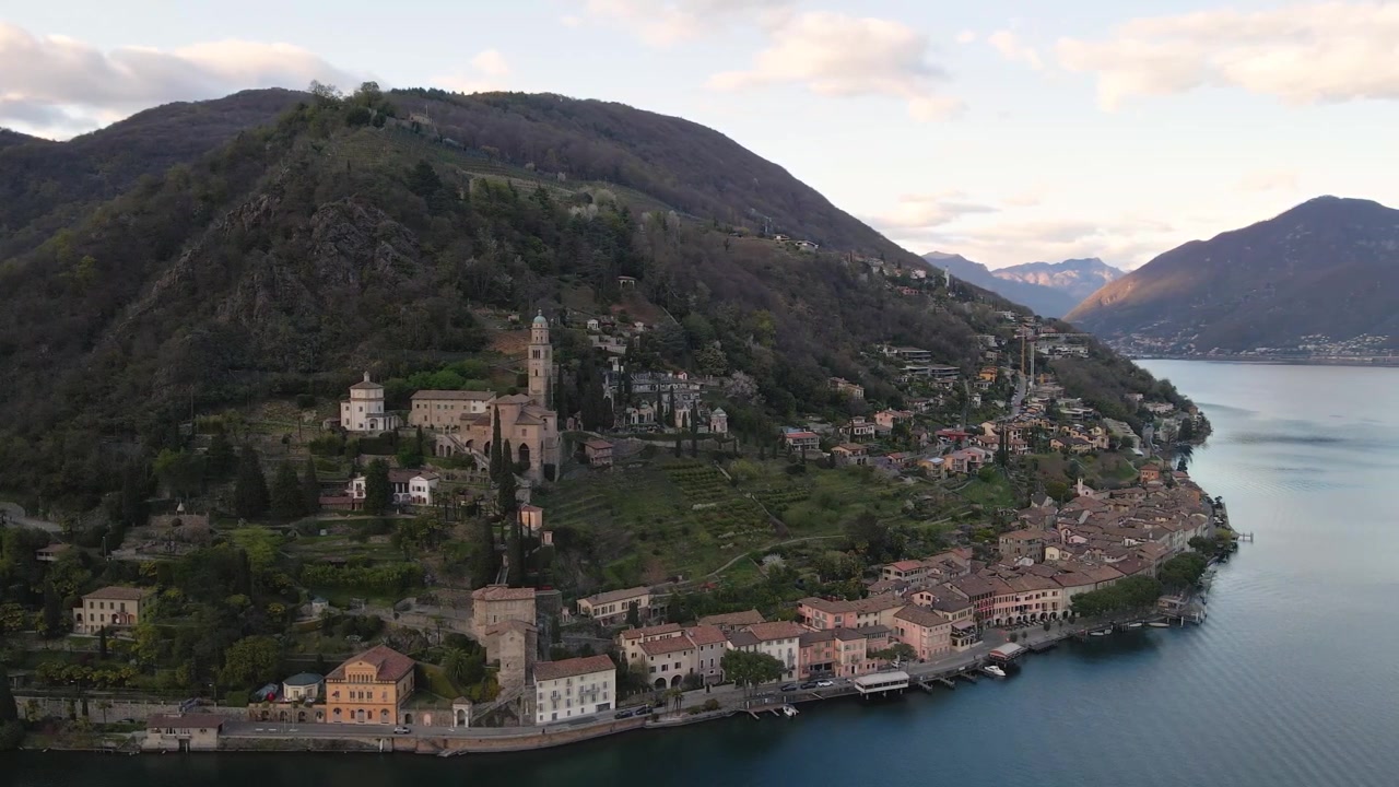 Pit­to­re­sco vil­lag­gio di Mor­co­te, adagiato sulle rive del lago di Lugano, con la sua iconica chiesa e le case tradizionali, circondato da una vegetazione lussureggiante e acque tranquille. Ticino, Svizzera, drone in orbita.