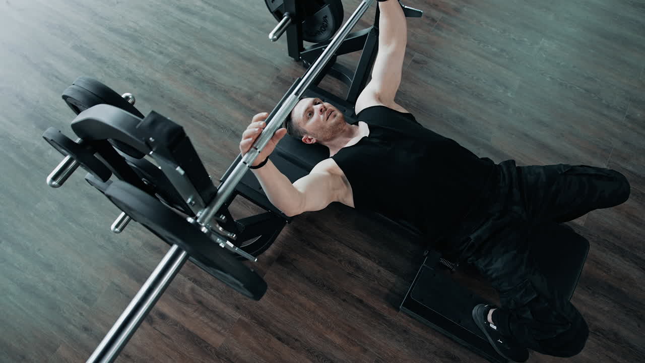 Strong healthy bodybuilder exercising in gym. Handsome guy lifting barbell while laying on a simulator. Top view. Sports concept.