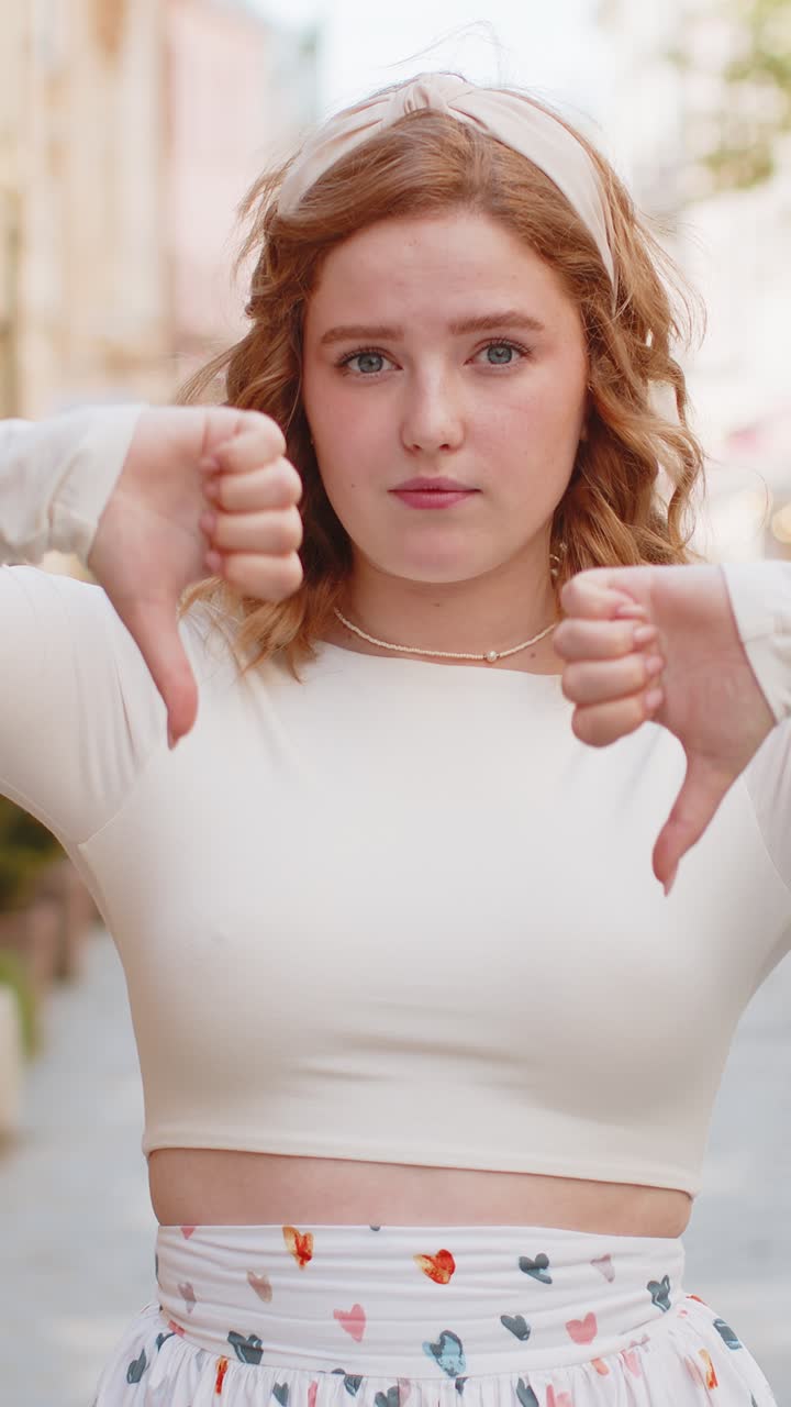 Upset redhead woman showing thumbs down sign disapproval dissatisfied bad work mistake in city
