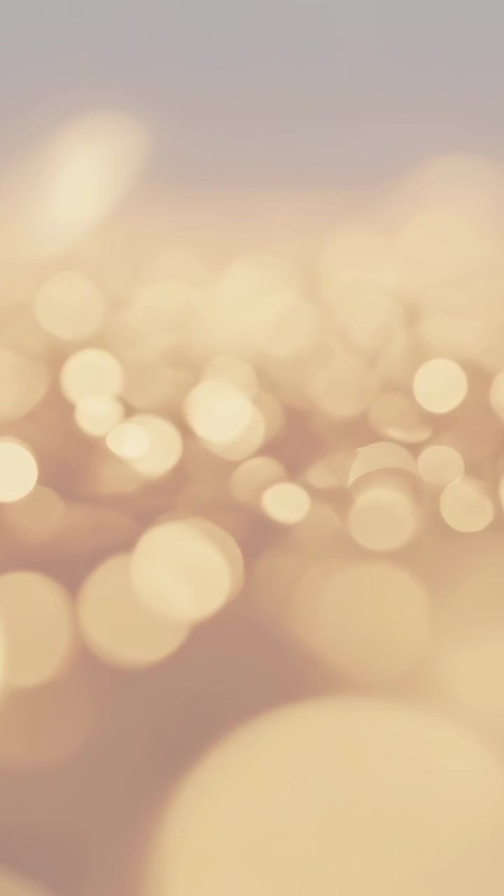 Vertical video: Playing golden bokeh shifting up-right in soft top gradient creating warm glow