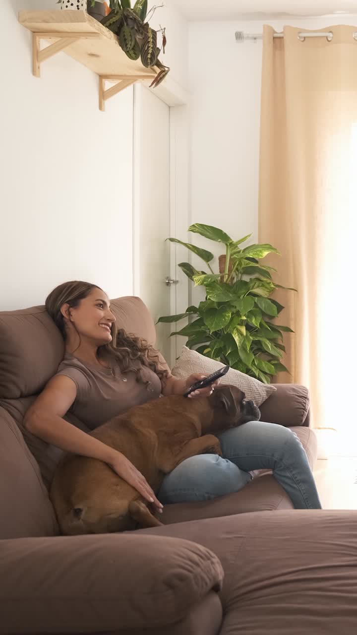Happy woman with Boxer dog watching TV in modern apartment