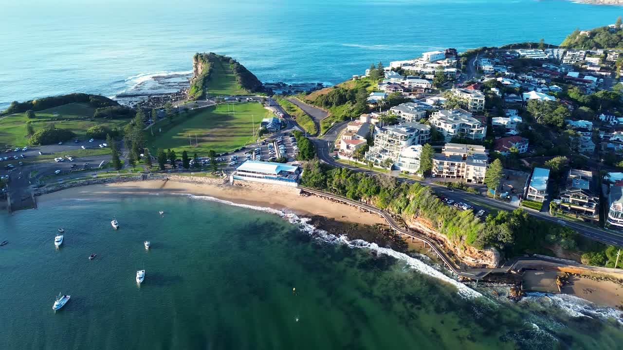 Drone aerial landscape of Terrigal suburban town with boats docked in The Haven beach bay waterfront with boardwalk and residential apartments housing Central Coast Australia travel infrastructure