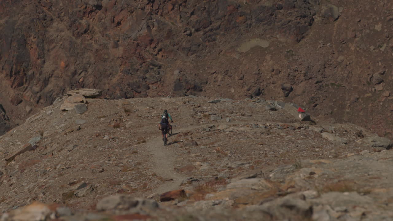 Two mountain bikers riding downhill on an alpine trail in Saas-Grund, Valais. Fast-paced descent, scenic Swiss mountain backdrop, and dynamic summer adventure sports atmosphere