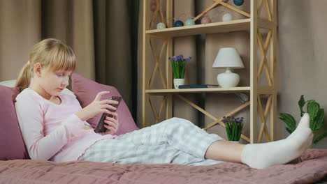 Blonde-girl-in-her-bed-uses-a-smartphone