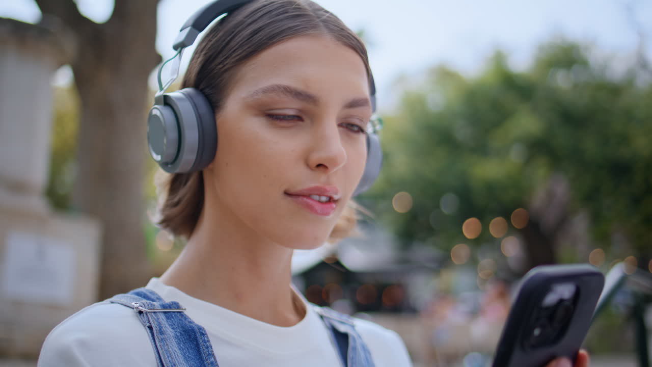 Girl posing street headphones holding mobile phone closeup. Woman listening song