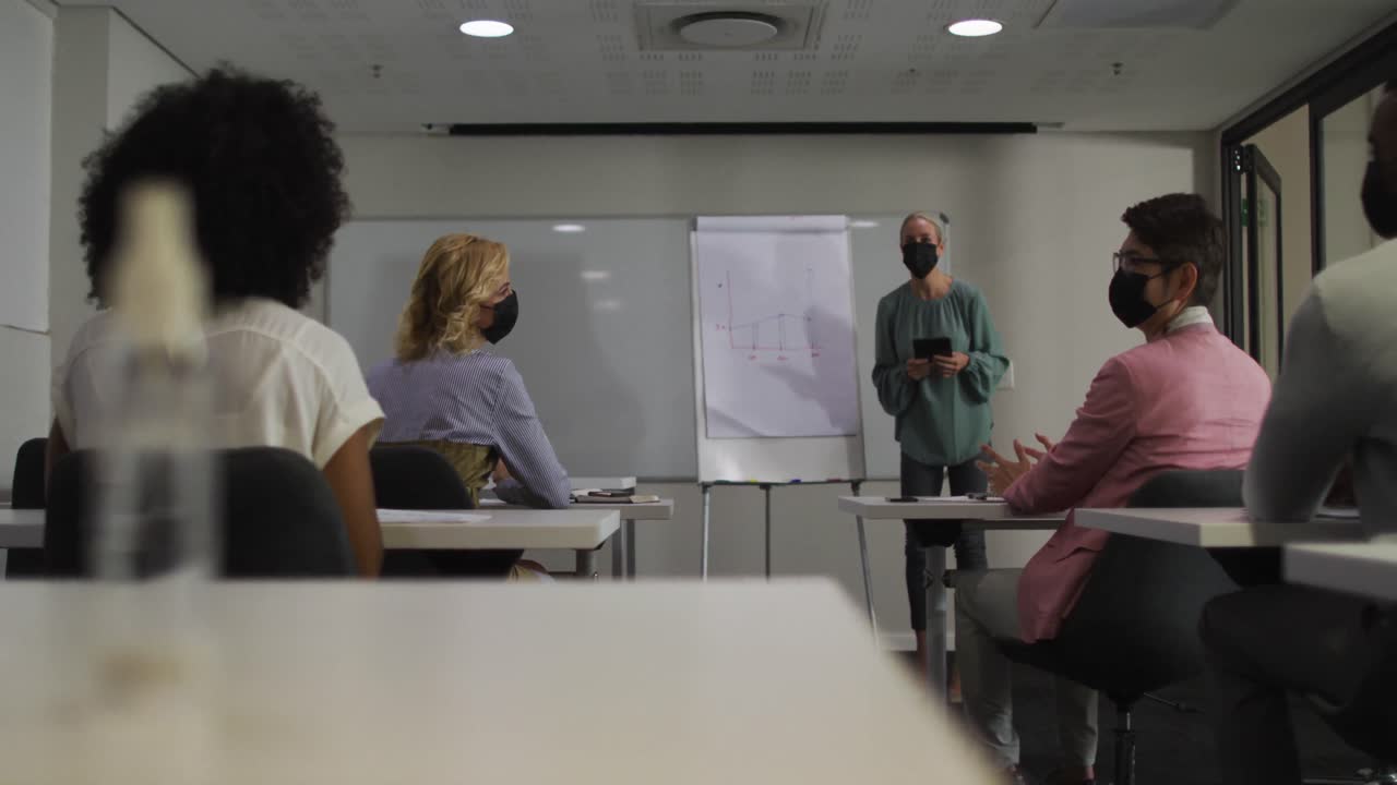 mujer de negocios caucásica con máscara dando una presentación a un grupo diverso de colegas