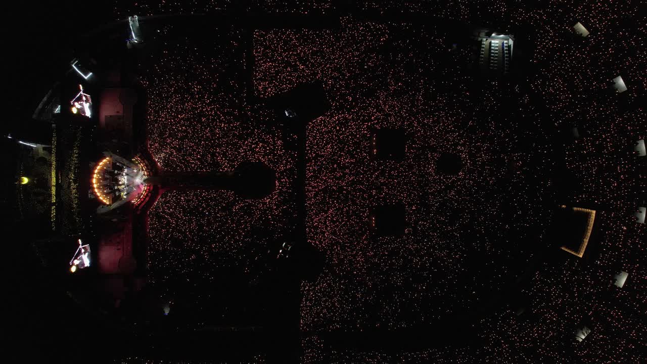 Luftfoto ovenfra af en koncert på et stort stadion med et lysshow skabt af tusindvis af fans.